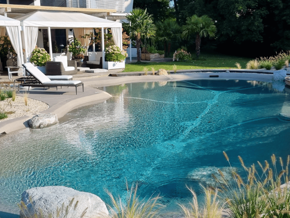 Grosszügiger BIO.design Pool vor Villa mit Terrasse, Palmen und gepflegtem Garten